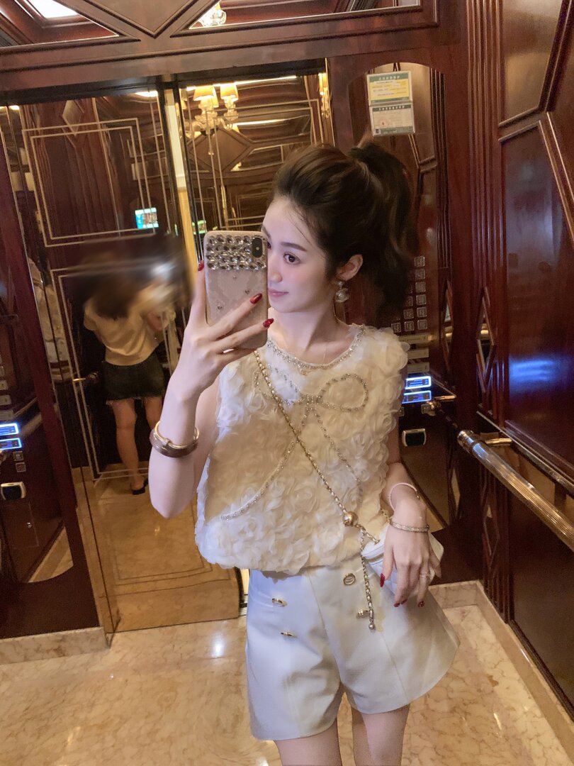 Woman wearing a white embellished sleeveless top and shorts in a mirror selfie