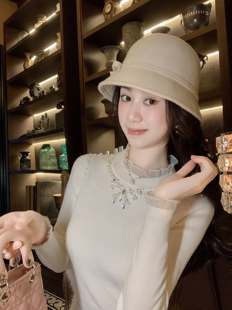 Woman wearing a cream knit sweater and matching bucket hat, holding a pink handbag