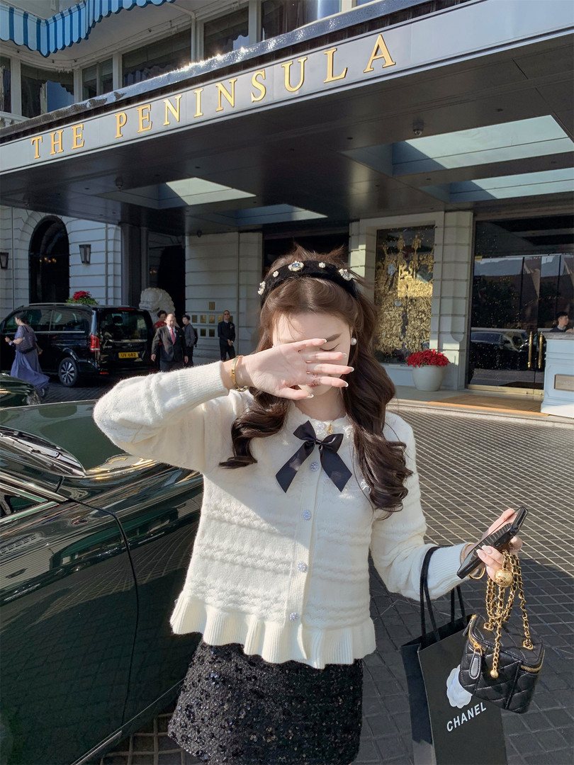 Woman wearing a cream cardigan and black skirt with a Chanel handbag outside The Peninsula hotel