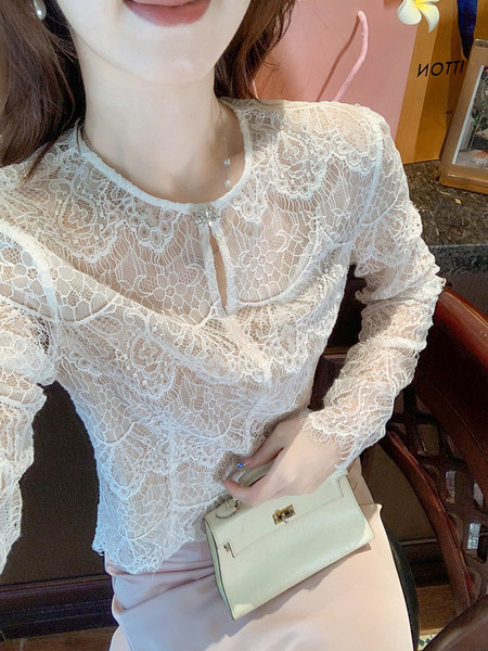 White lace long-sleeve blouse worn by a model with a small cream handbag