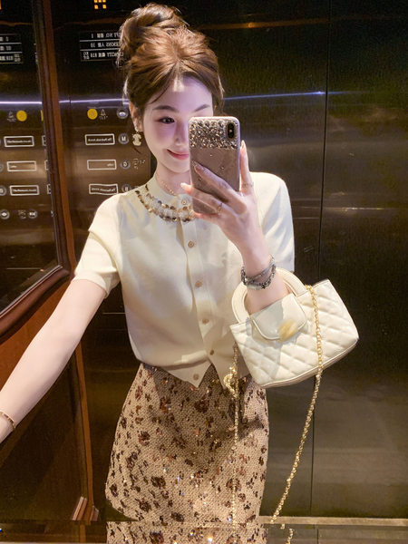 Woman wearing a cream short-sleeve cardigan and floral skirt holding a white quilted handbag