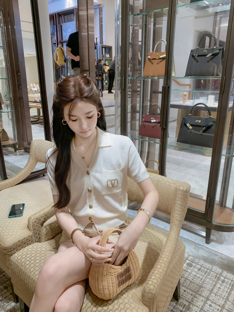 Woman wearing a white short-sleeve buttoned knit top and holding a woven handbag