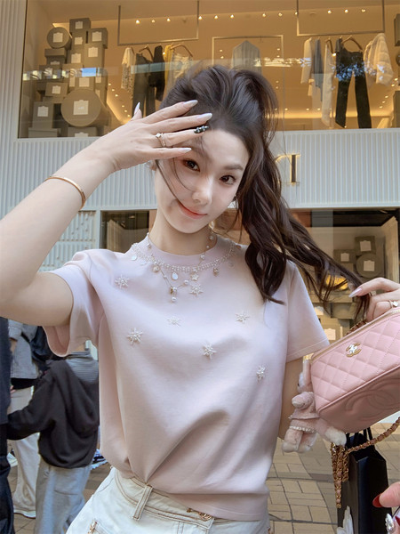 Woman wearing a light pink embellished short-sleeve top and holding a pink quilted handbag