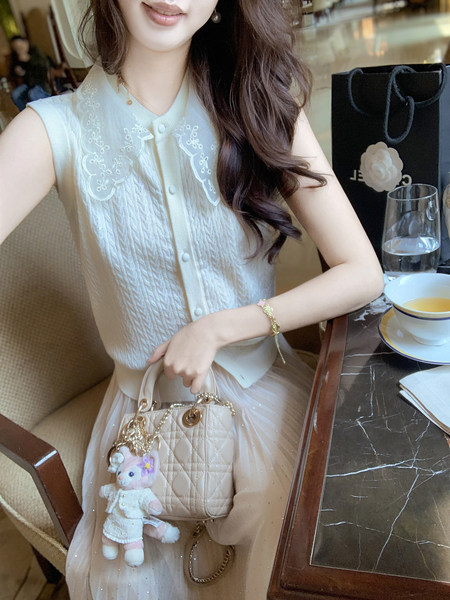 Woman wearing a white sleeveless lace-trim top and holding a quilted handbag