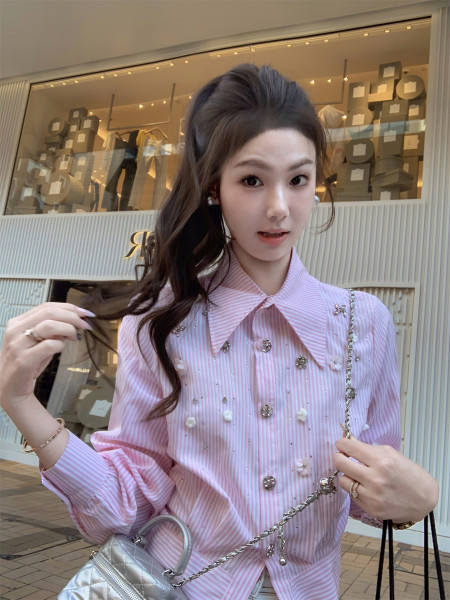 Woman wearing a pink striped embellished blouse and holding a silver quilted handbag
