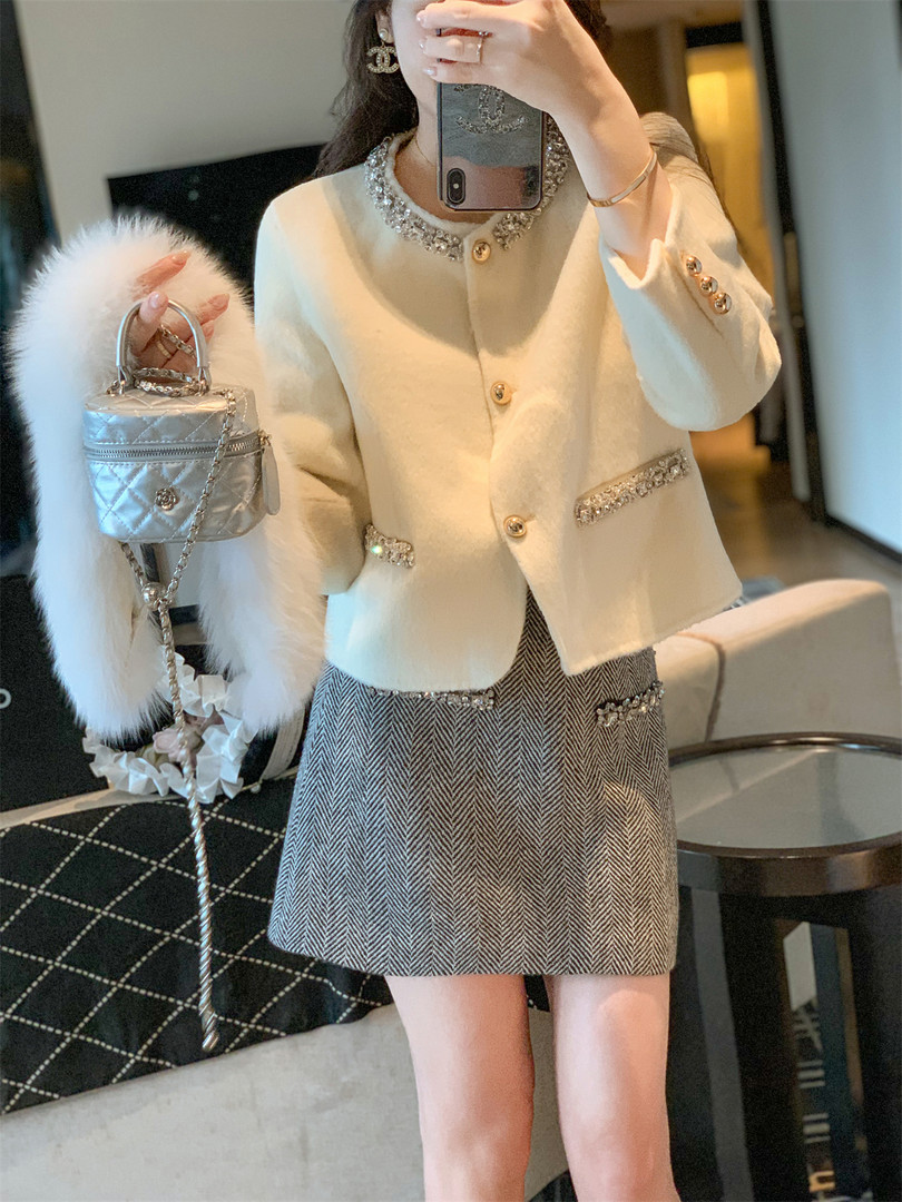 Woman wearing an embellished cream jacket with a herringbone mini skirt and holding a silver handbag