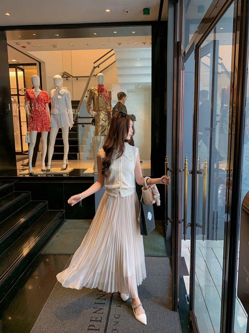 Woman modeling a cream sleeveless top with a pleated skirt in a boutique entrance