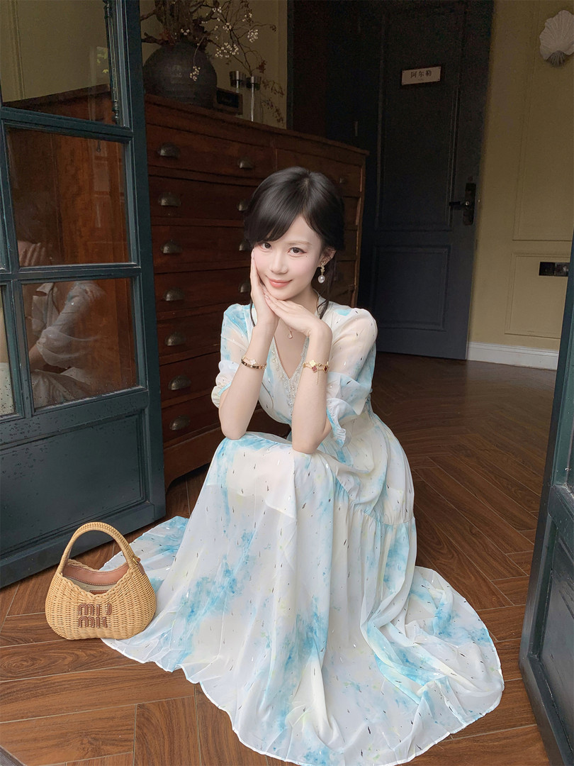 Woman wearing a light blue and white flowy dress with a woven handbag