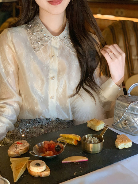 Woman wearing a sheer embellished blouse with a jeweled collar at a table