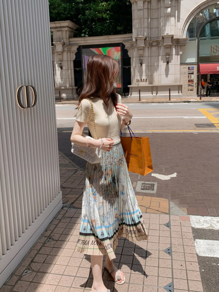 Woman wearing a beige top and pleated printed midi skirt on a city street