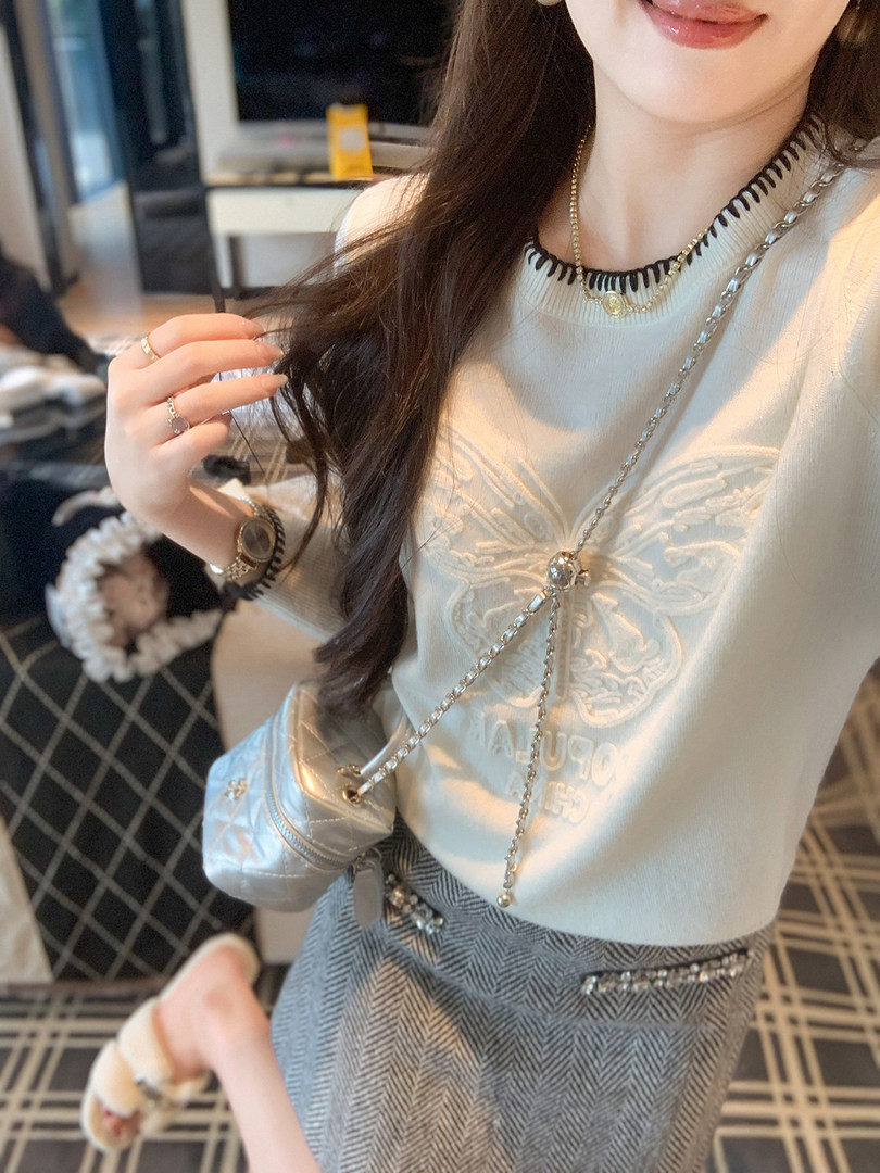 Young woman wearing a white knit top with chain details and a herringbone skirt