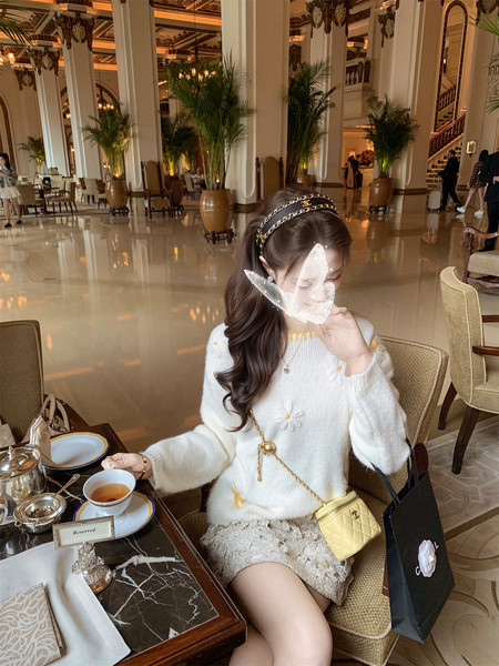Woman wearing a white sweater and lace skirt with a yellow quilted handbag at a café.