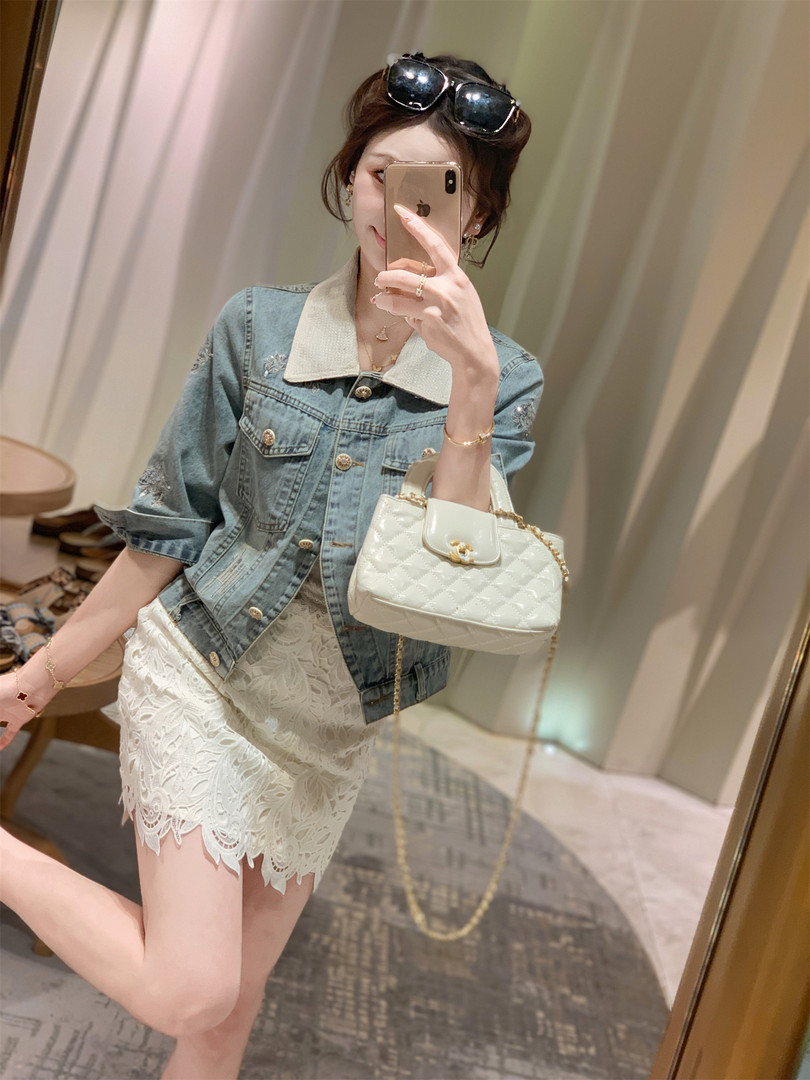 Woman wearing a denim jacket and white lace skirt with a white quilted handbag