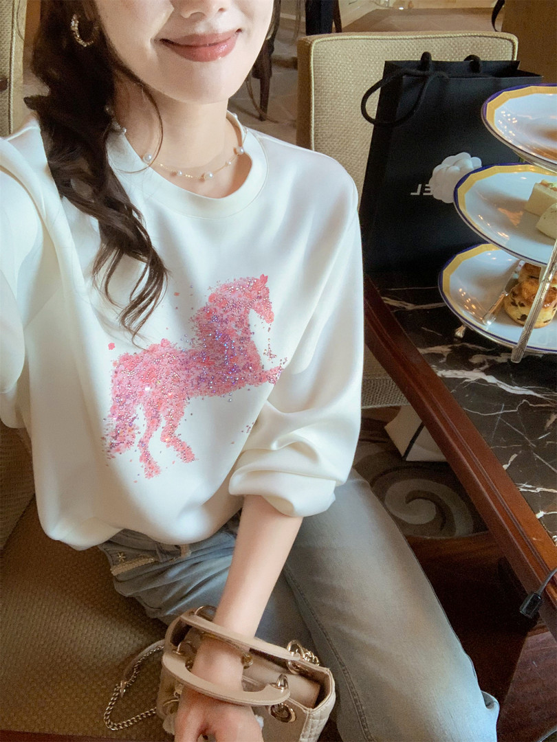 Woman wearing a white oversized sweatshirt with a pink glitter horse graphic