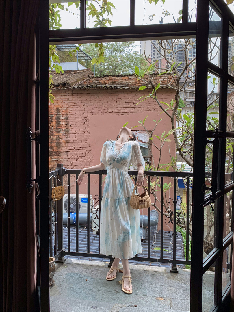 Woman wearing a light blue and white flowy midi dress with a woven handbag and sandals