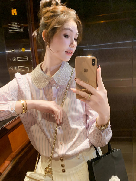 Woman wearing a pastel striped blouse with a pearl collar and cream skirt