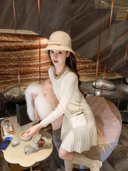 Woman modeling a cream outfit with a hat, pleated skirt, boots, and a small crossbody bag