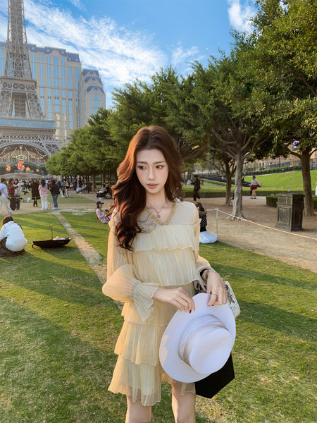 Woman wearing a light yellow pleated dress outdoors with a white hat