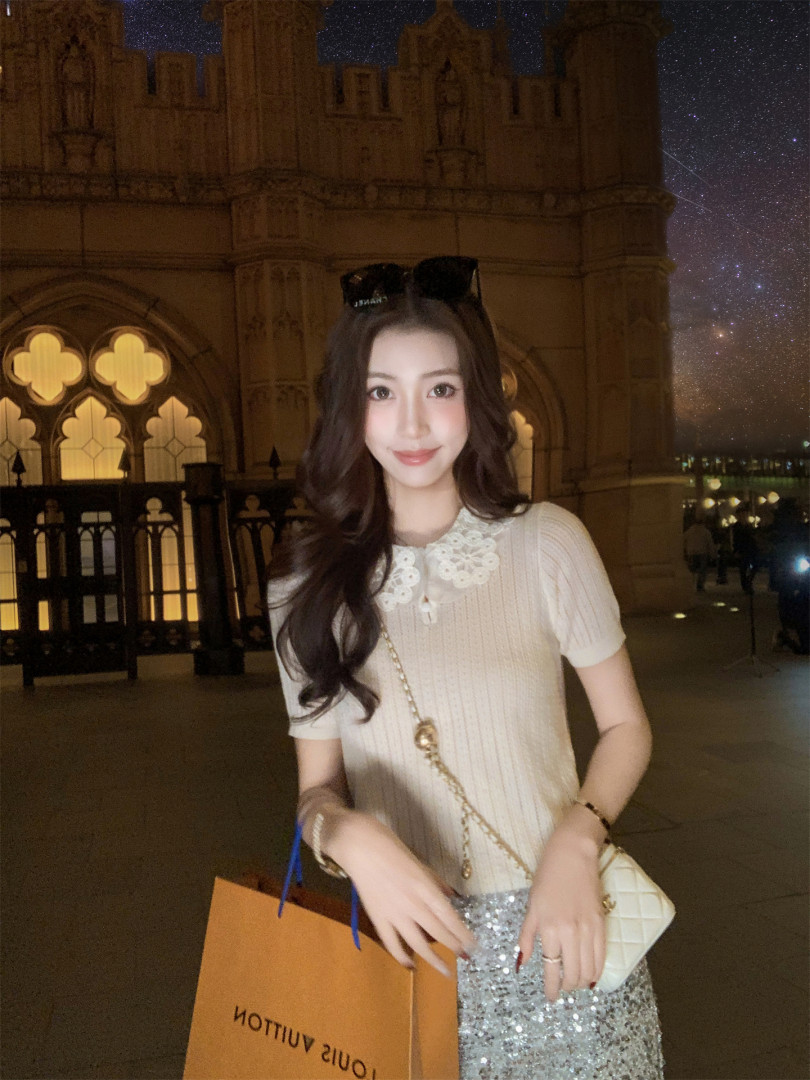 Woman wearing a cream knit top with lace collar and a sparkly skirt, carrying shopping bags and a quilted handbag