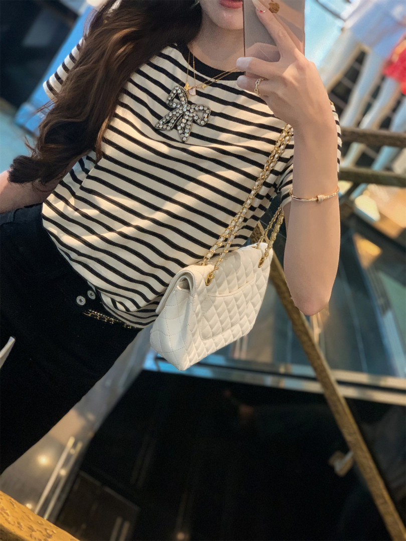 Woman wearing a black-and-white striped top with a quilted white chain-strap shoulder bag