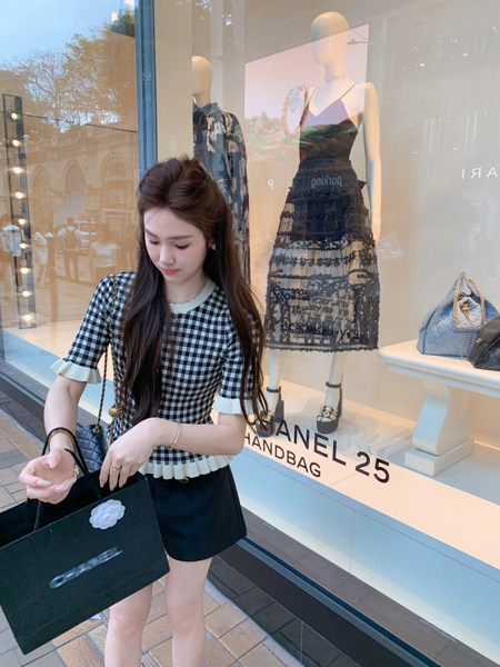 Woman wearing a black-and-white checkered short-sleeve top with black shorts outside a luxury storefront