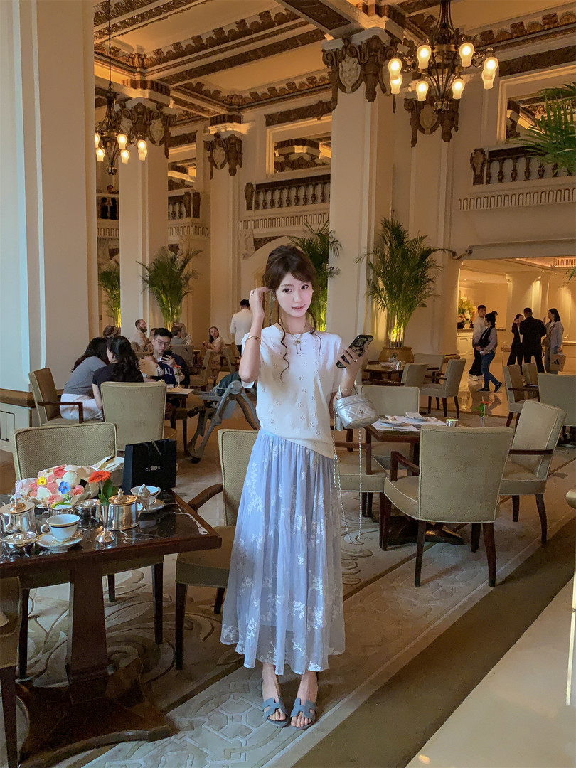 Woman wearing a white top, light blue skirt, and blue sandals in a hotel lounge