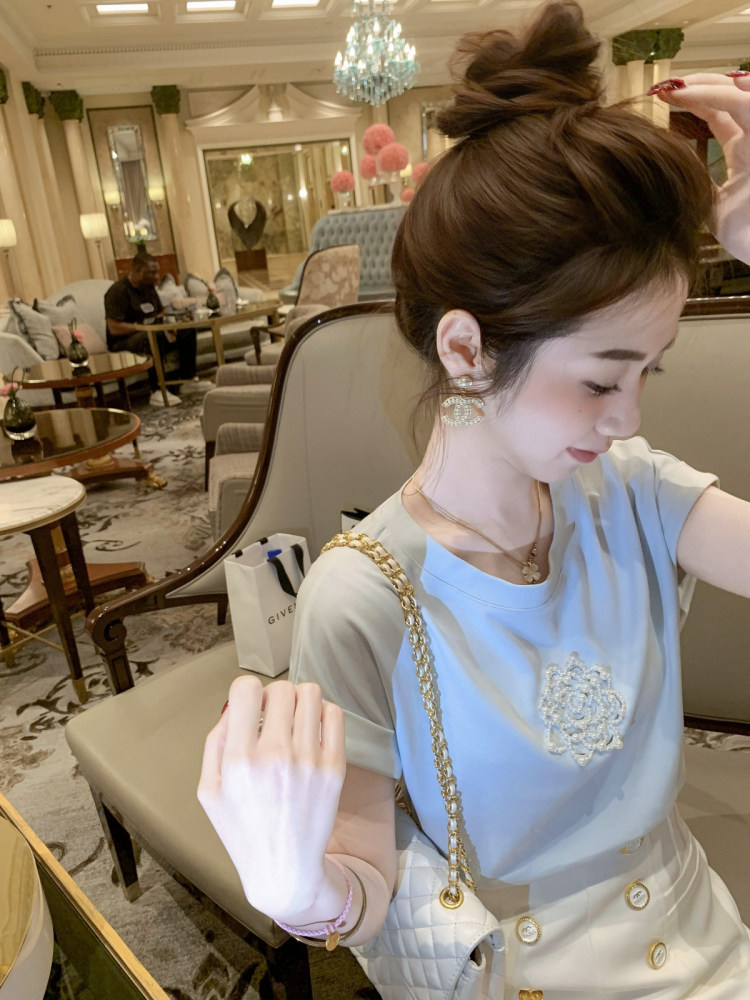 Woman wearing a light blue embellished top and white skirt with a gold chain bag