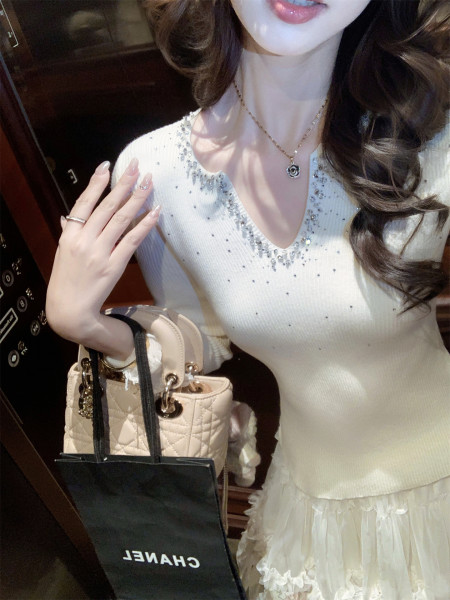 Woman wearing a white embellished knit top and layered skirt with a quilted handbag