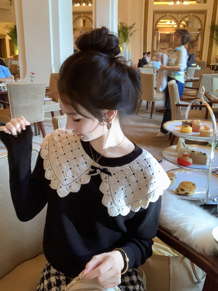 Woman wearing a black sweater with a large white lace collar in a restaurant