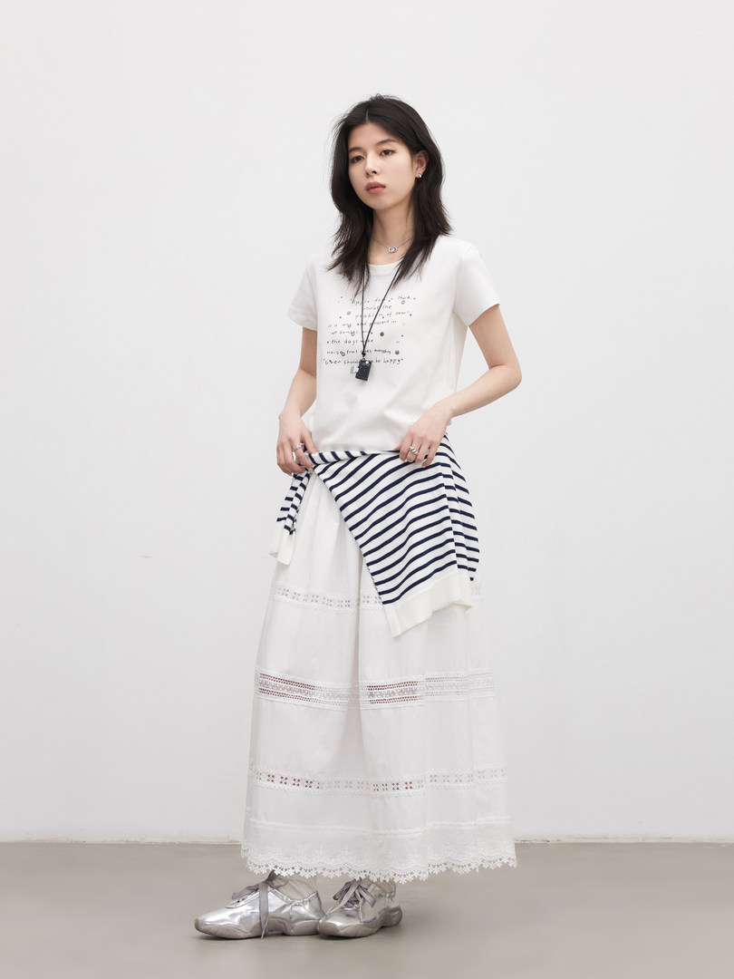 Model wearing a white graphic T-shirt with a striped sweater tied at the waist and a white lace maxi skirt