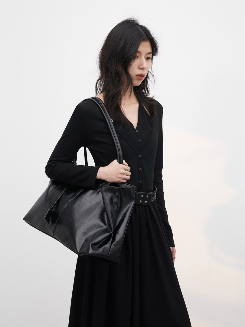 Woman wearing a black long-sleeve dress and carrying a black leather tote bag