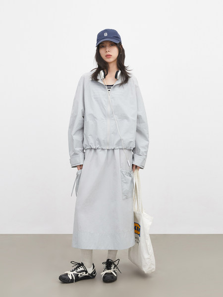 Model wearing a light gray layered outfit with cap, jacket, and long skirt