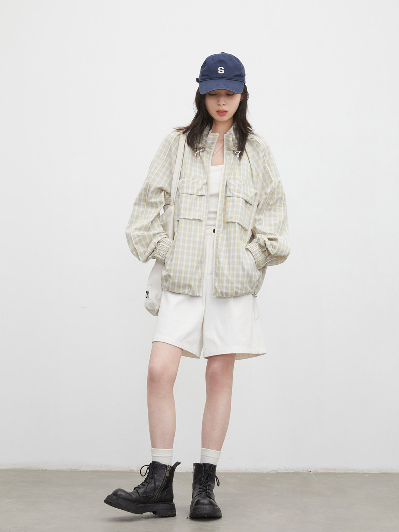 Model wearing a light plaid jacket, white shorts, black boots, and a navy cap
