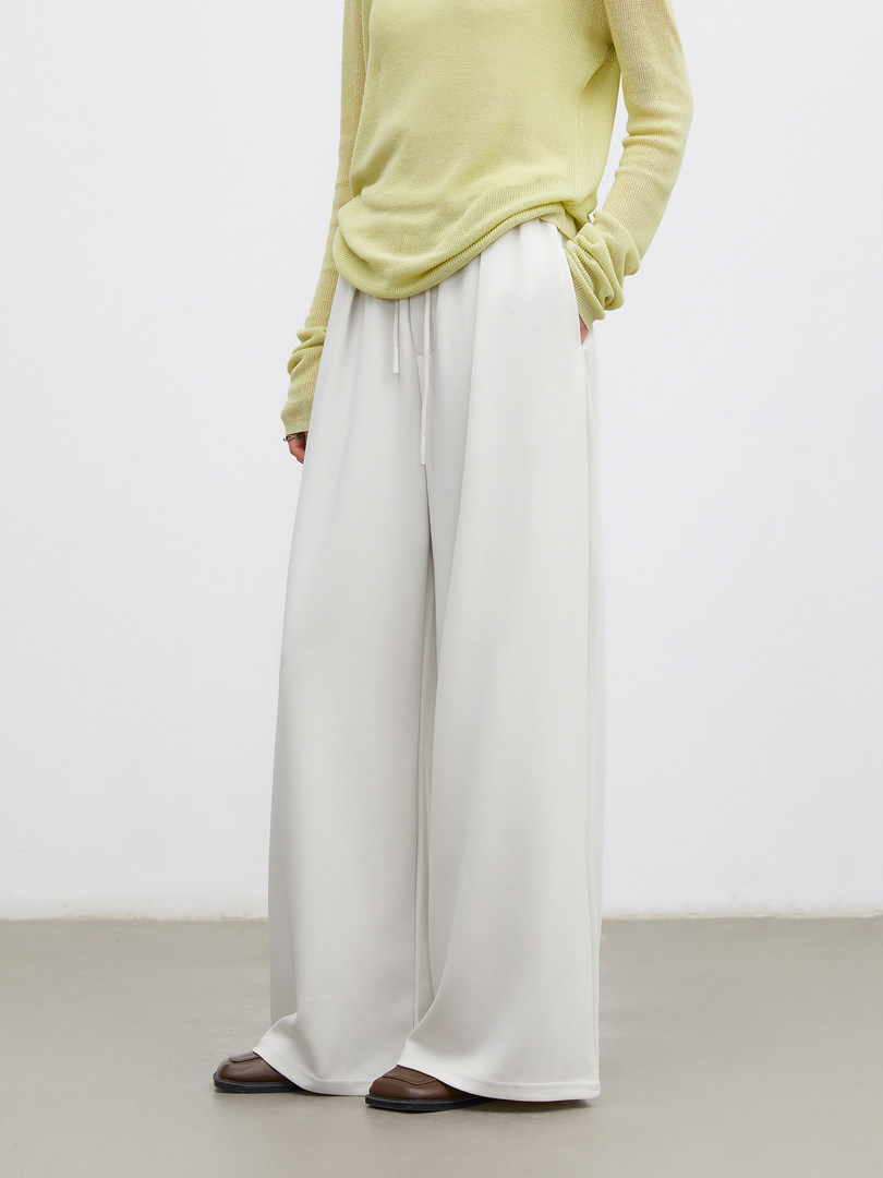 Model wearing a pale yellow sweater with wide-leg white pants and brown shoes