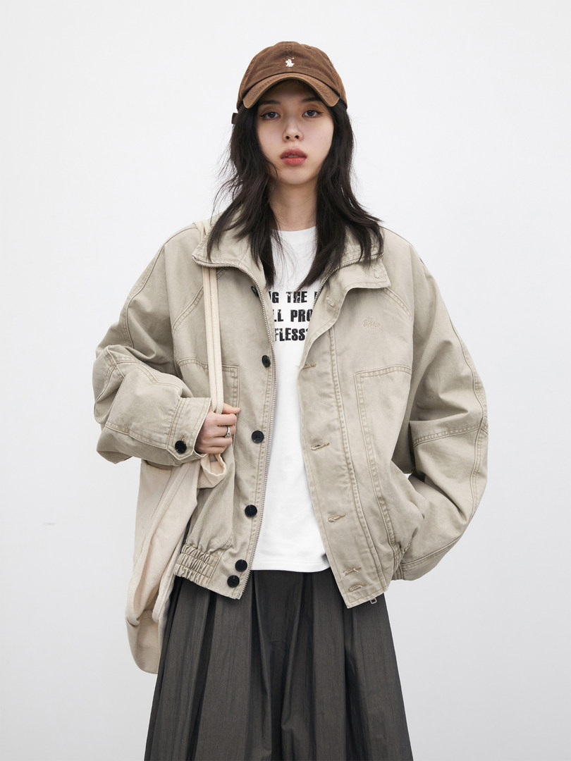 Model wearing a beige oversized jacket with a brown cap and tote bag