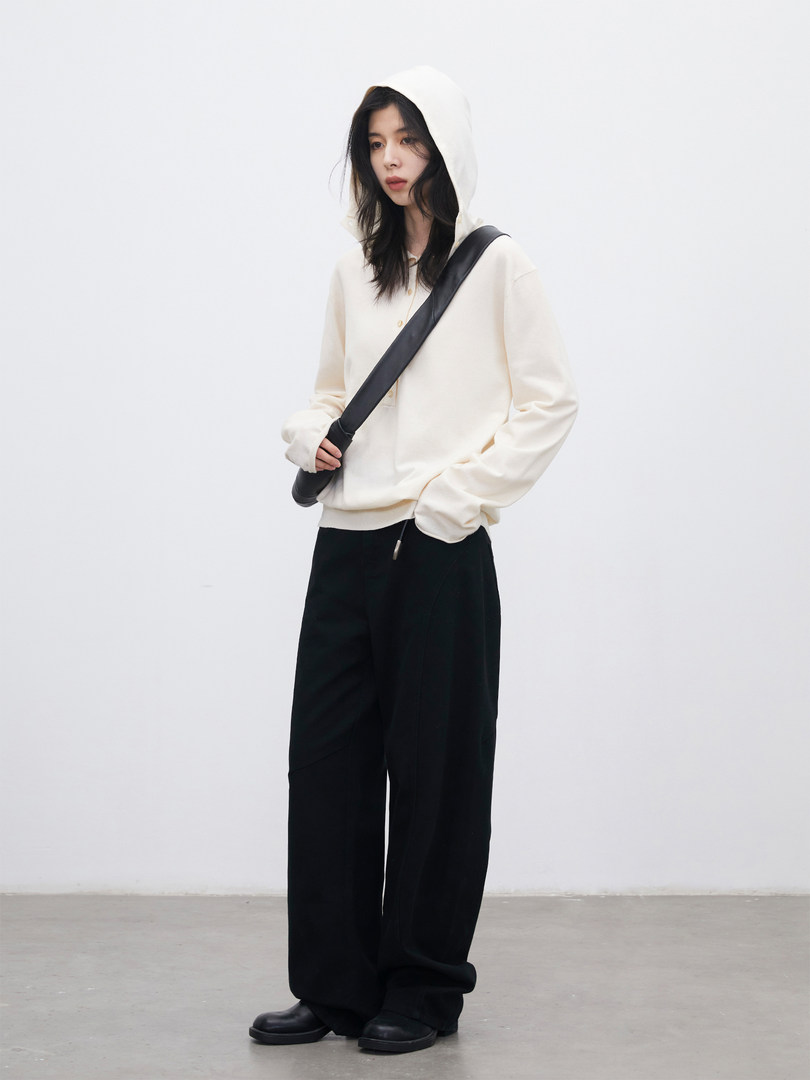 Model wearing a cream hooded sweatshirt with black wide-leg pants and a black crossbody bag
