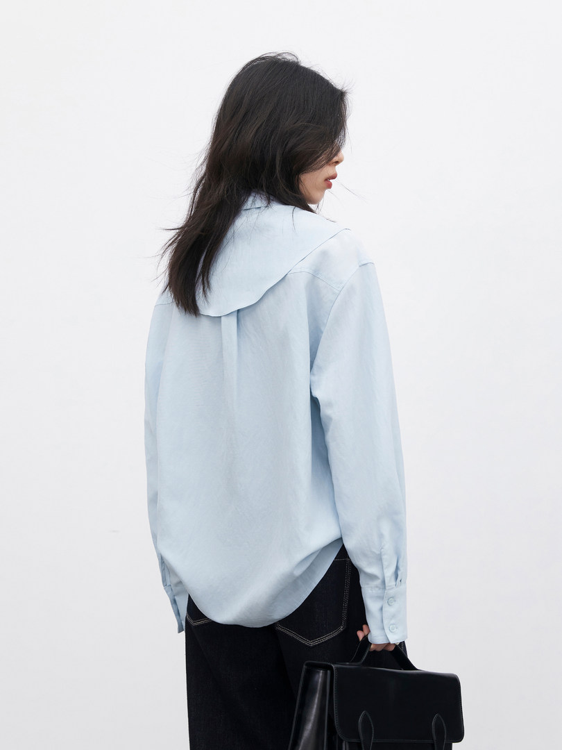 Model wearing a light blue long-sleeve shirt and holding a black handbag