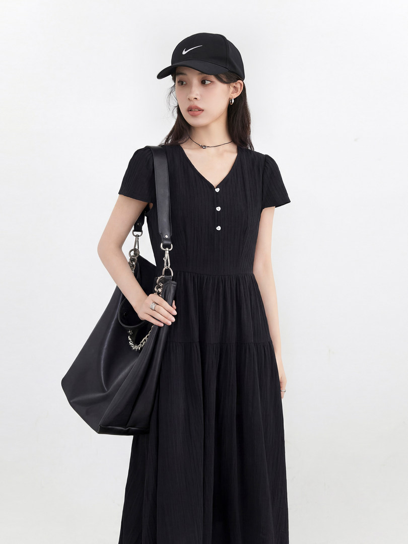 Black short-sleeve midi dress worn by a model with a black cap and shoulder bag