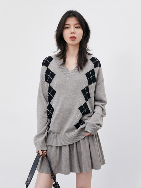 Model wearing a gray argyle V-neck sweater with a matching pleated skirt
