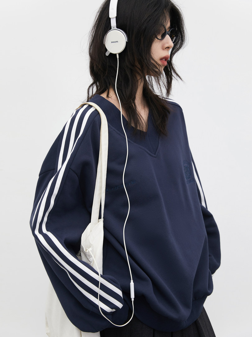 Model wearing a navy oversized striped sweatshirt with white headphones and a tote bag