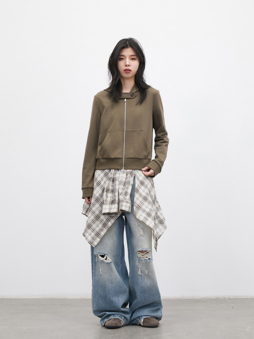 Model wearing layered streetwear outfit with olive zip jacket, plaid shirt, and distressed wide-leg jeans