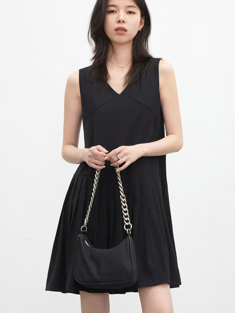 Black sleeveless dress worn by a model, paired with a chain-strap handbag