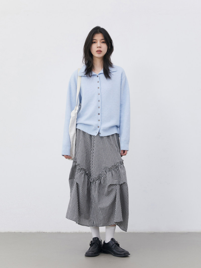 Model wearing a light blue button-up cardigan with a black-and-white gingham skirt and black loafers