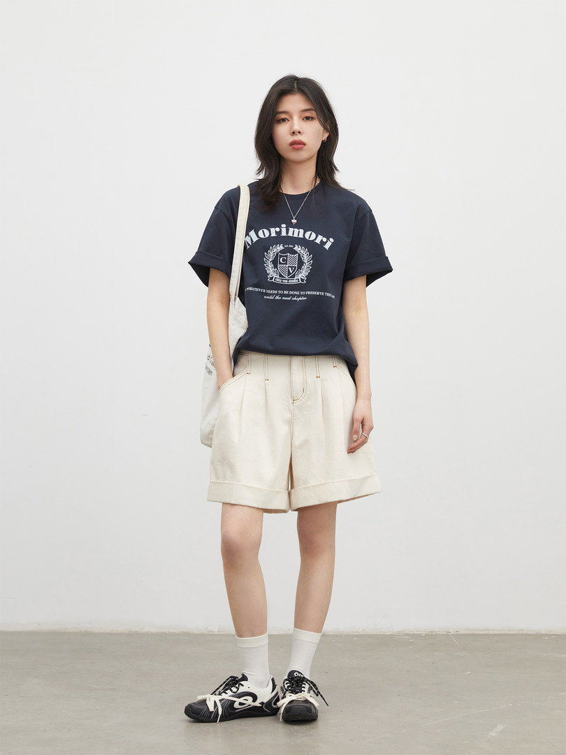 Model wearing a navy graphic T-shirt, cream shorts, and sneakers
