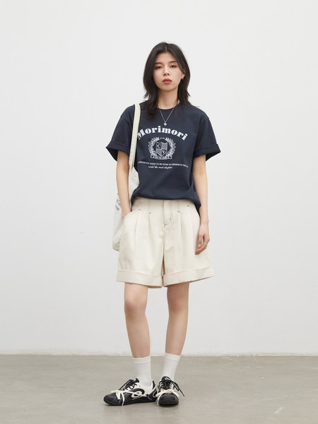 Model wearing a navy graphic T-shirt, cream shorts, and sneakers