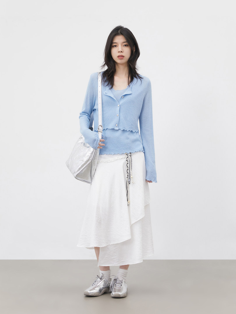 Model wearing a light blue buttoned cardigan with a white asymmetrical skirt and silver sneakers