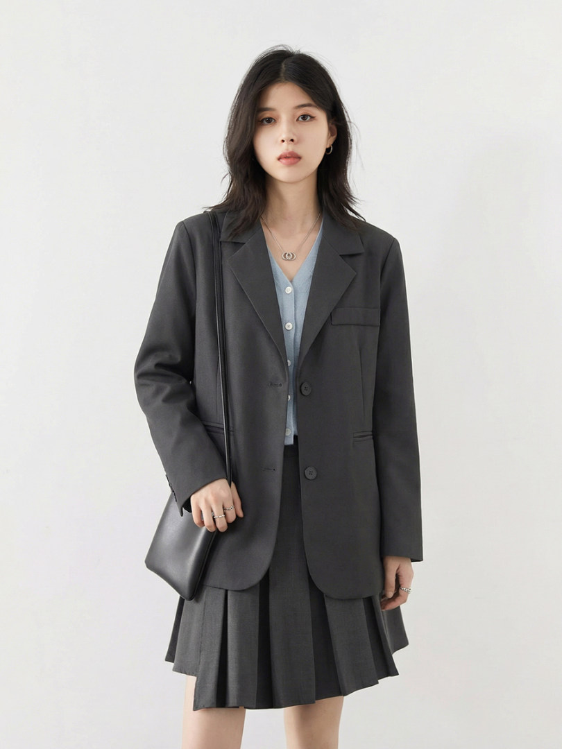 Model wearing a dark blazer and pleated skirt with a light blue top and black shoulder bag