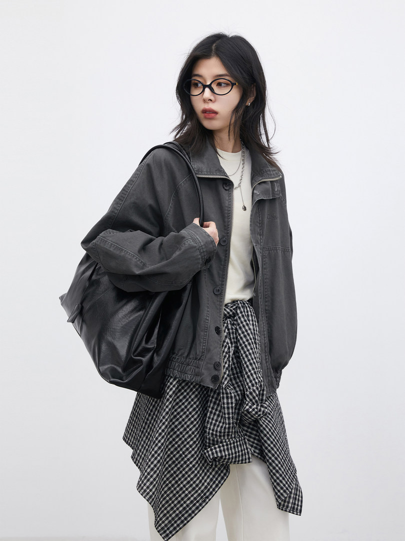 Model wearing a dark gray jacket layered over a checkered shirt and white top