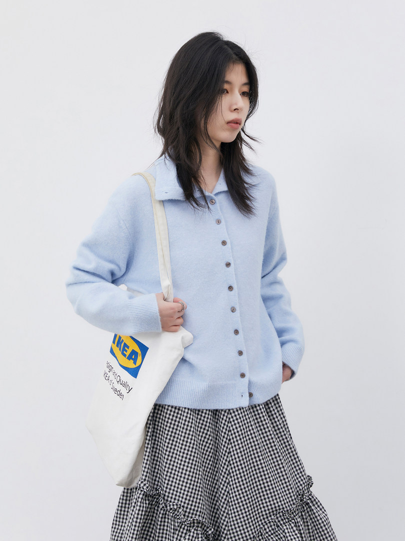 Model wearing a light blue button-up cardigan with a gingham skirt and tote bag