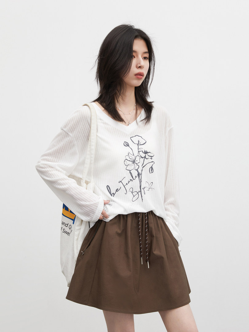 Model wearing a white long-sleeve graphic top and brown skirt